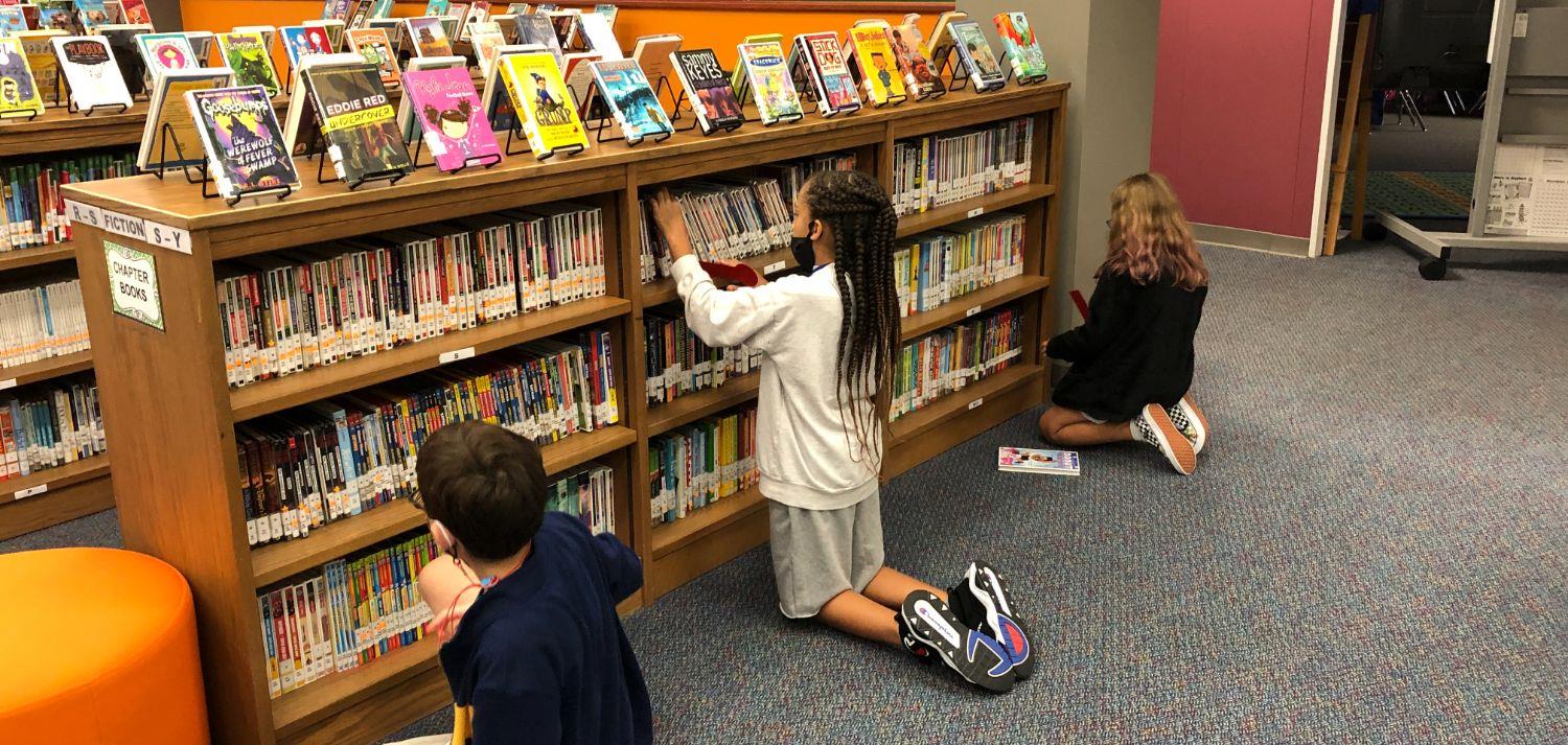 3 students looking at books on shelves